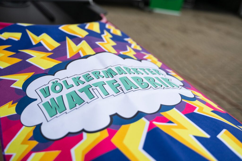 Bunt beklebtes Ruderboot mit der Aufschrift „Völkermarkter Wattfabrik“, gestaltet im Comic-Stil mit Blitzen und kräftigen Farben.